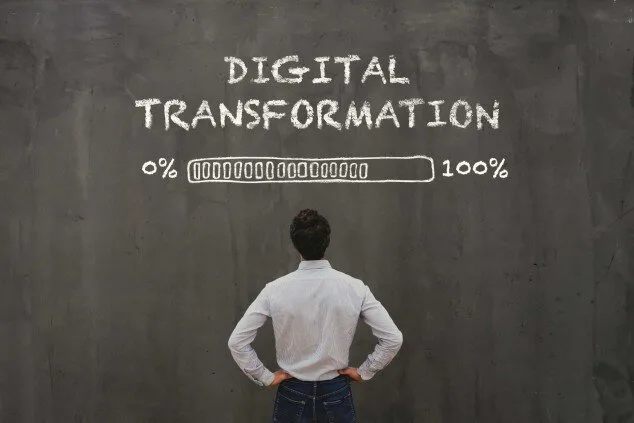 A man faces a chalk wall reading Digital Transformation above a progress bar from 0% to 100%