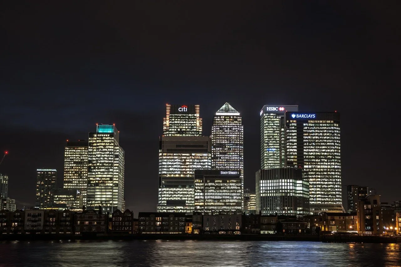 Canary Wharf office towers in London lit up at night, seen across the River Thames