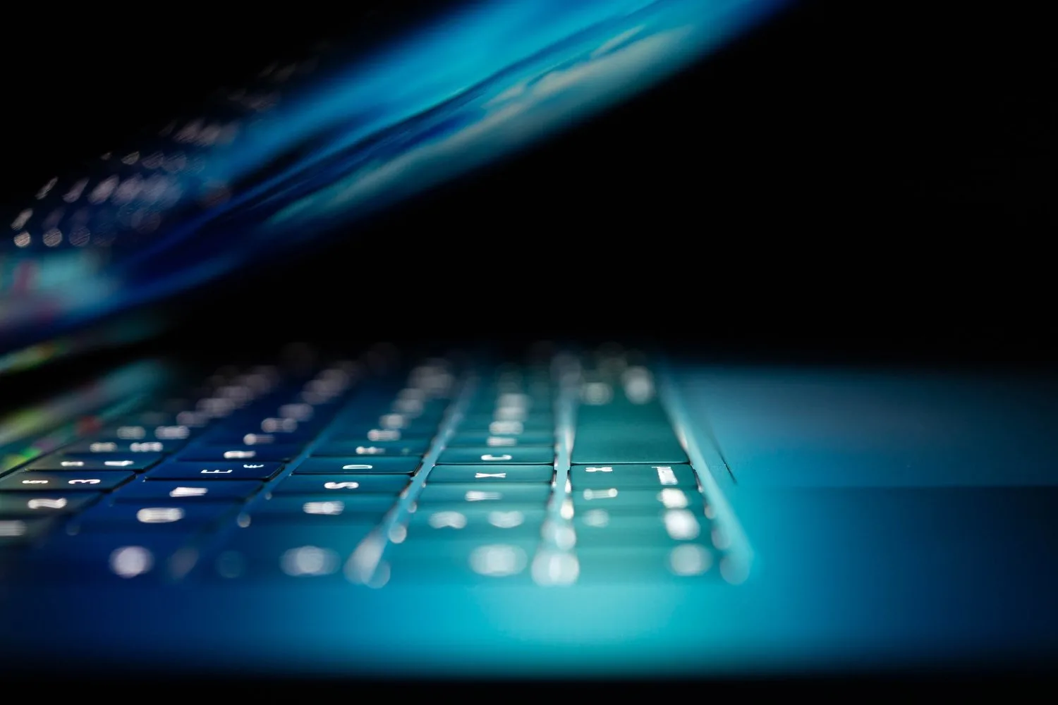 Close-up of a laptop keyboard lit by the blue glow of its screen in the dark